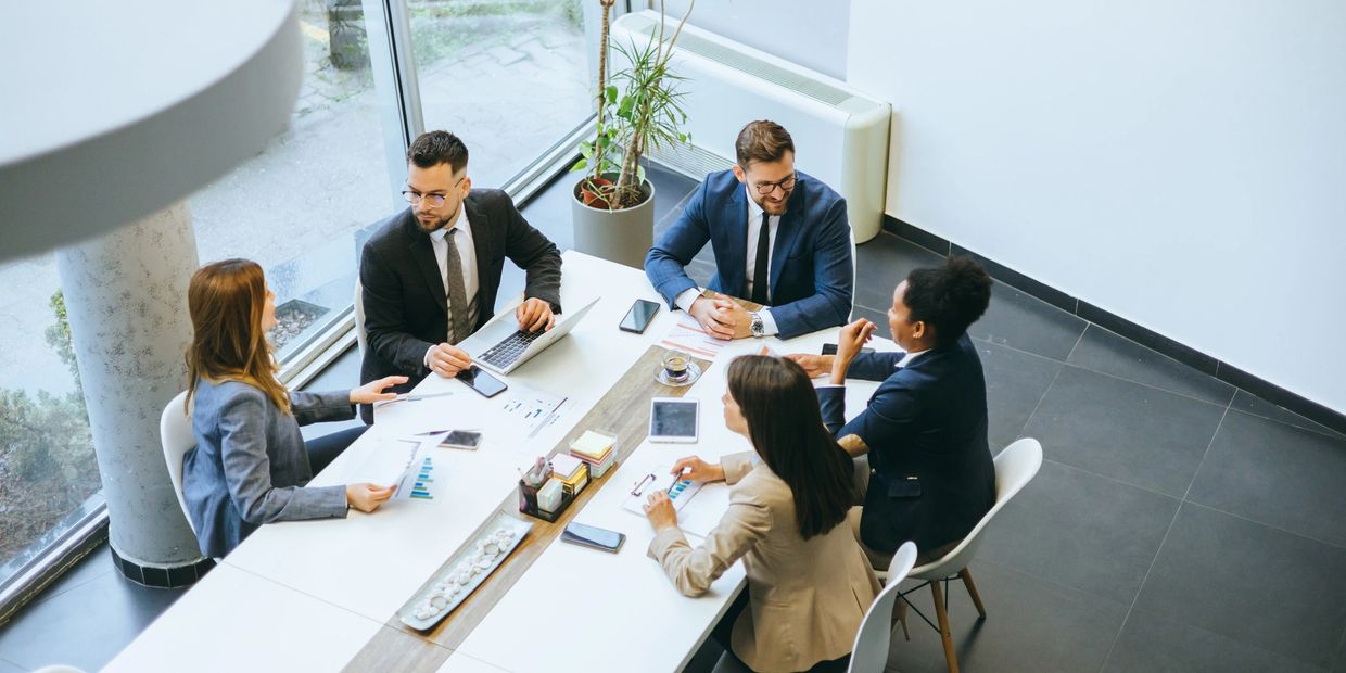 Five professionals in a business meeting around a modern table.