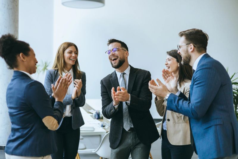 A joyous business colleague receives applause from a business team in an office setting