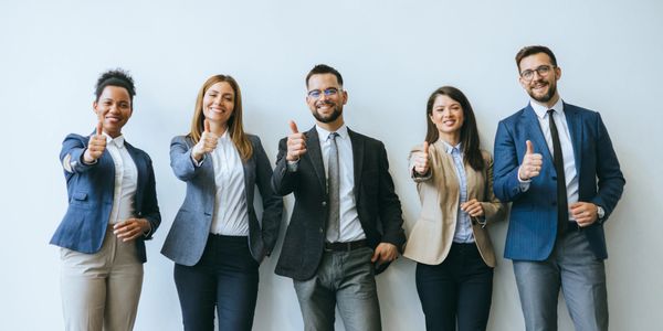Five professionals in business attire giving thumbs up and smiling.