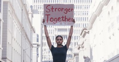 Woman holding a sign that reads 'Stronger Together' in the city.