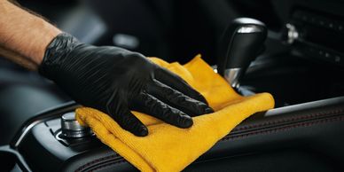 Hand with black glove cleaning car interior with yellow cloth.