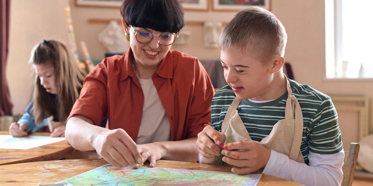 Teacher helping a boy with drawing in a classroom.