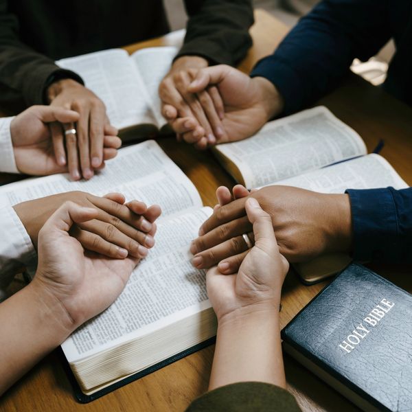 People holding hands in prayer around open Bibles.