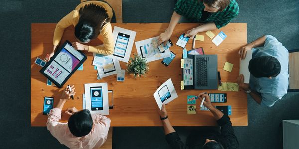 A team collaborates on mobile app design using sketches and digital devices around a wooden table.