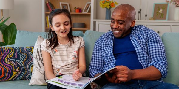 A happy girl and man reading a book together on a couch.