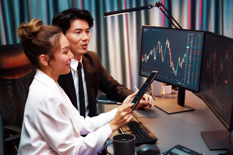 Businesswoman holding tablet on dynamic stock exchange statistic online showing to partners to share, comparing with high or low point graph on computer screen at night neon modern office. Infobahn.
