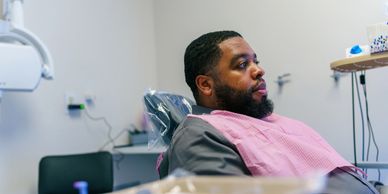 Man sitting in a dental chair wearing a pink dental bib.