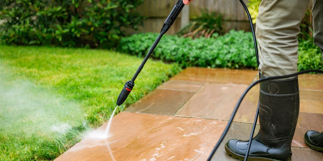 Professional cleaner using a pressure washer to clean a paved patio area outside a property.
