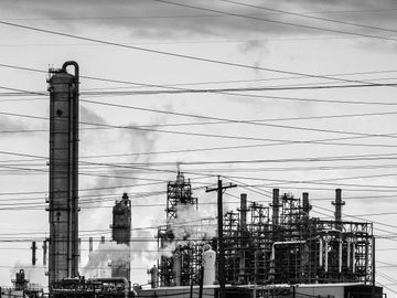 Black and white photo of an industrial refinery with smoke and power lines.