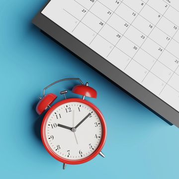 Red alarm clock and calendar on blue surface.