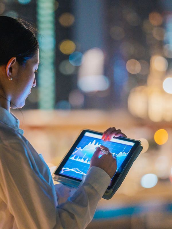 Woman using a tablet at night with city lights in the background.