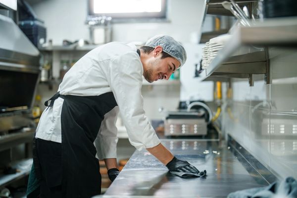 Chef cleaning stainless steel countertop in commercial kitchen.