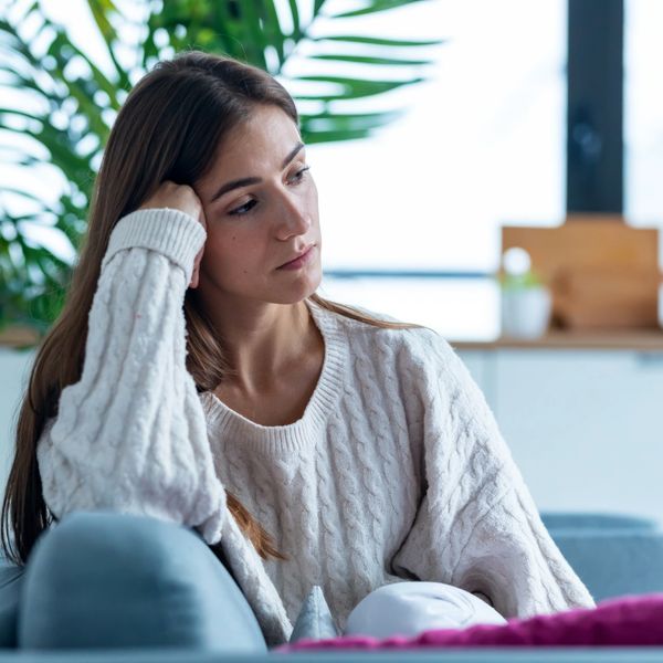 A woman in a white sweater looks thoughtful and pensive on a couch.