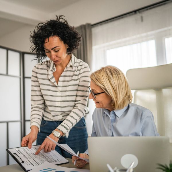 Two women discussing documents in a bright office setting.