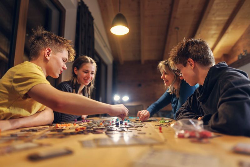 Mother and teenage kids playing large board game on the table. They are having fun, talking and laughing.Shot with Canon R5