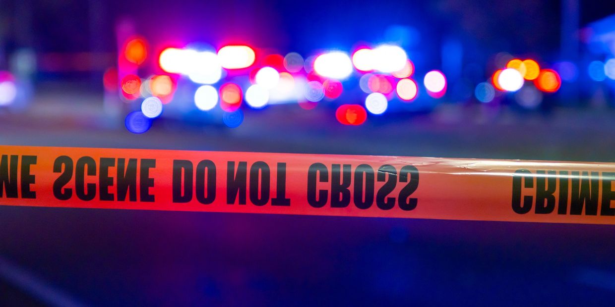 Police crime scene tape blocking off a blurred emergency scene at night.