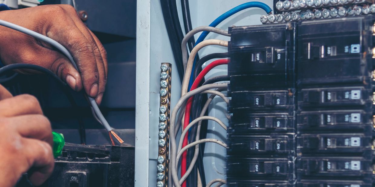 Hands working on electrical panel wiring.