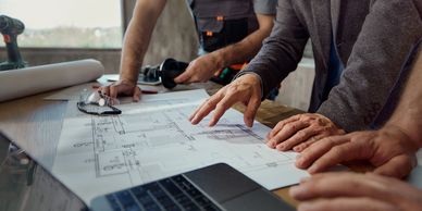 People reviewing architectural blueprints on a table with tools and a laptop.