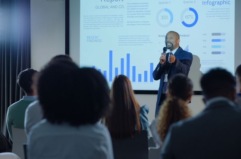 Black man, screen and audience for speech, conference and presentation for business in South Africa. Businessman, mic or ppt for analytics, infographic or data of financial review at convention