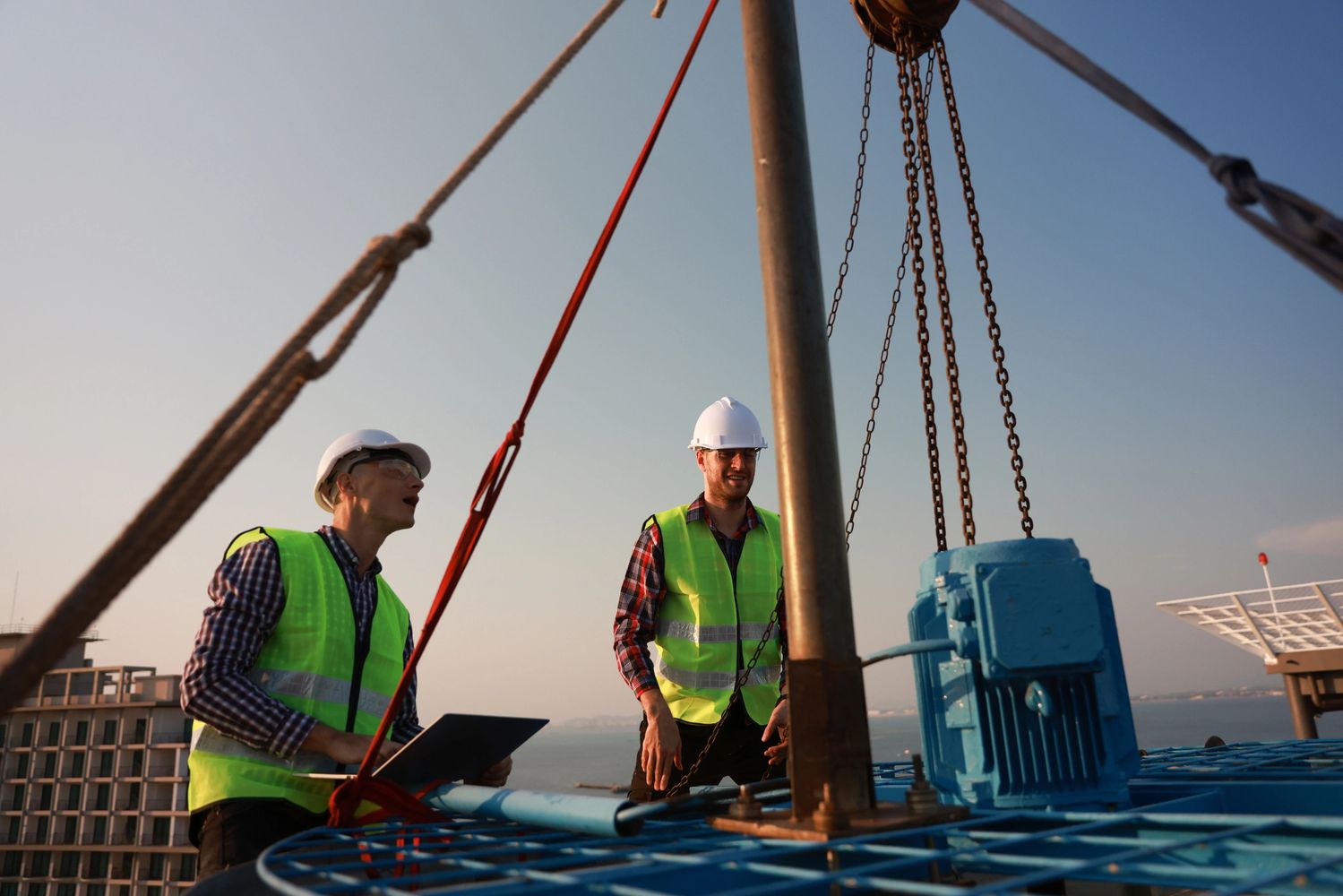 Two engineers in safety gear inspecting industrial machinery outdoors.