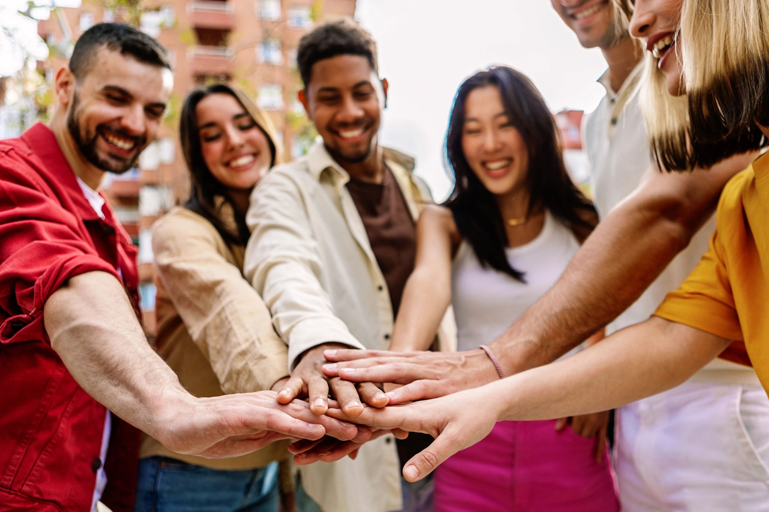A group of diverse friends joining hands and smiling outdoors.