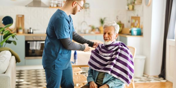Caregiver assisting elderly man in a living room.