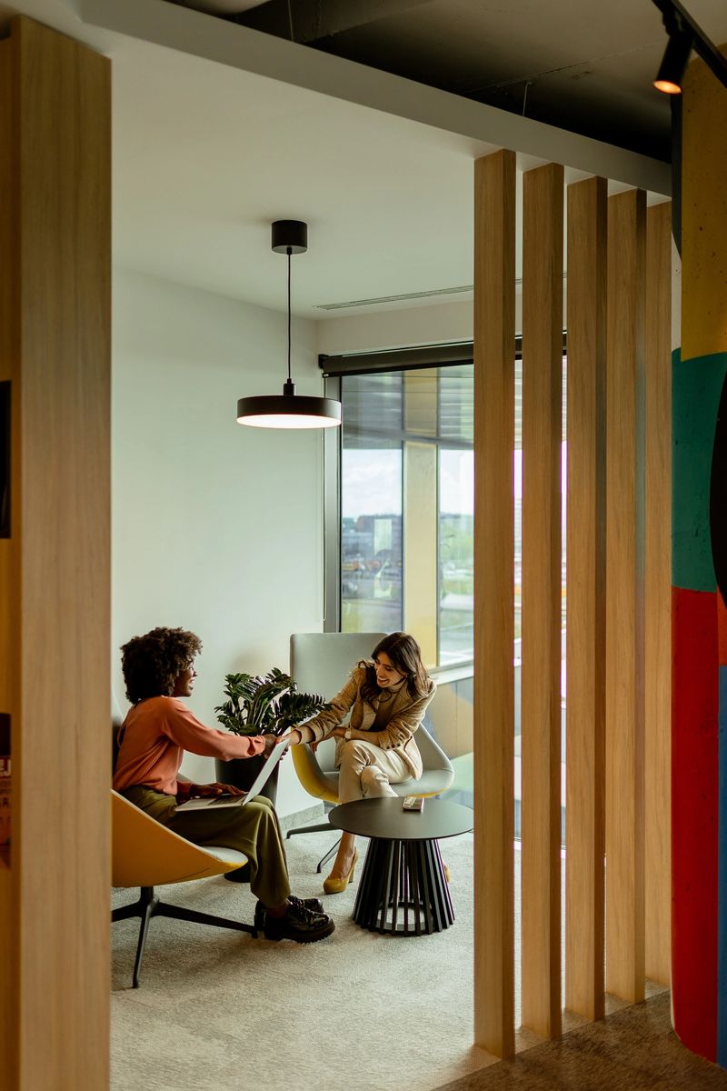 A warm, sunlit living room sets the scene for two friends enjoying a quiet conversation, exuding comfort and companionship