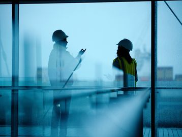 Two construction workers talk inside a building.