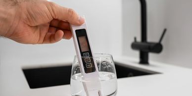 Hand holding a digital water quality tester in a glass of water.