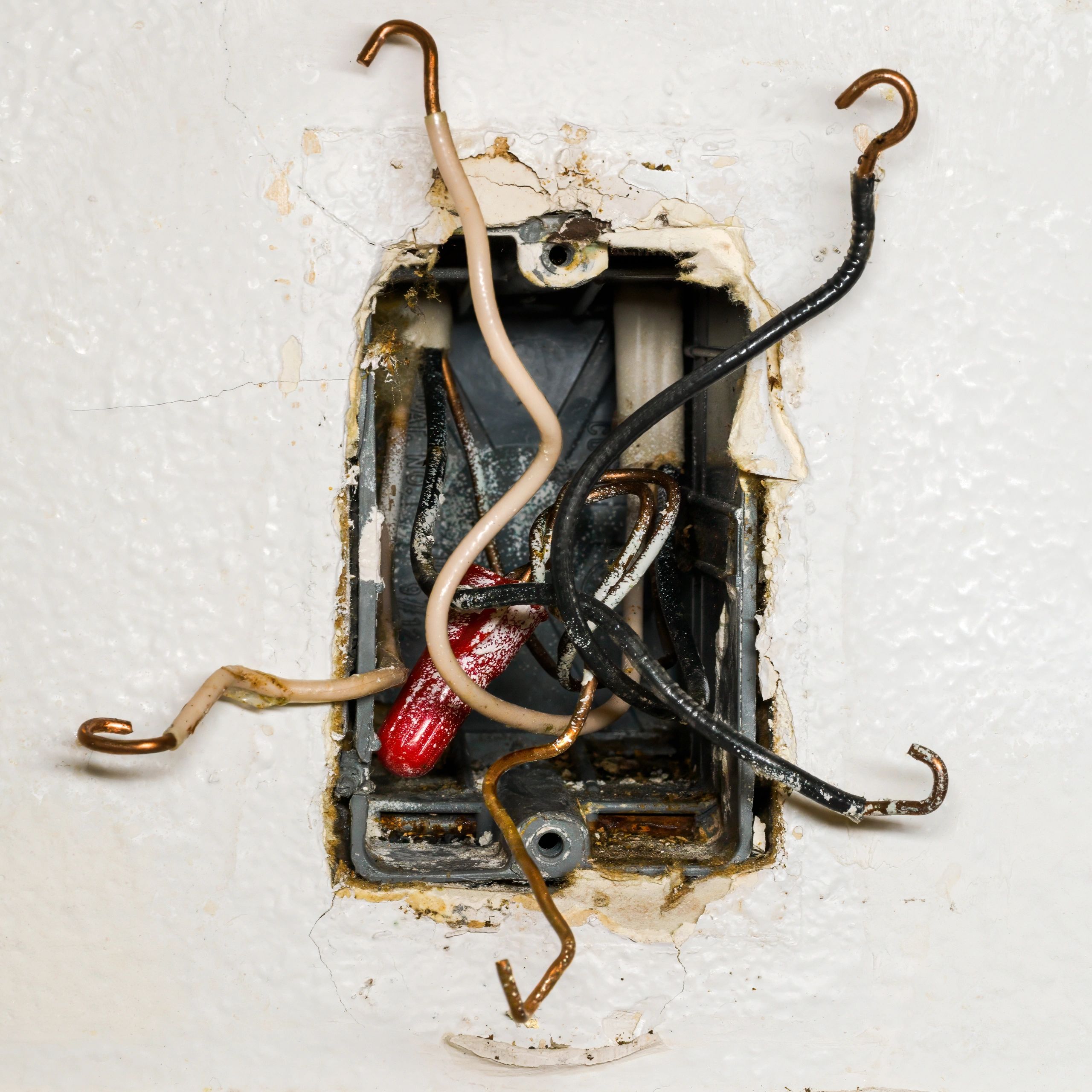 Exposed electrical wires protruding from a damaged wall outlet.