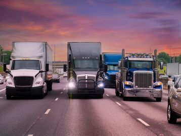 Three trucks lined up on a highway at sunset.