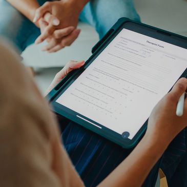 A therapist holds a tablet with a digital therapist form, interviewing a couple.