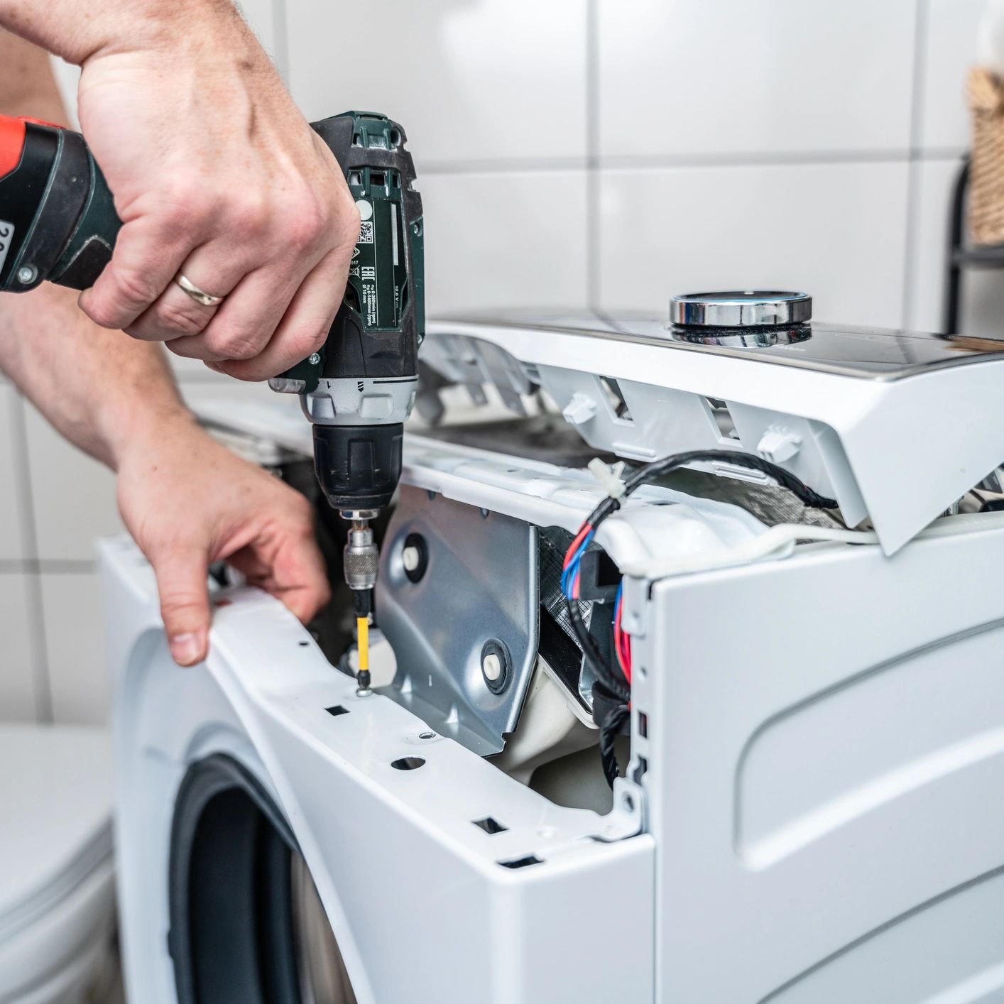 Person using a drill to repair a washing machine.