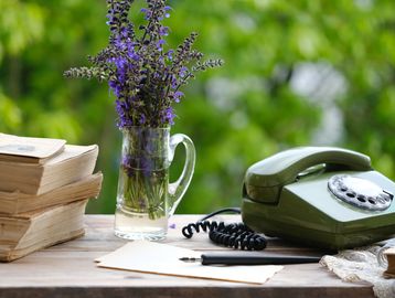 Vintage rotary phone, lavender bouquet, and old books on a wooden table.