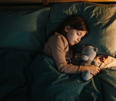A child peacefully sleeping while hugging a teddy bear in bed.