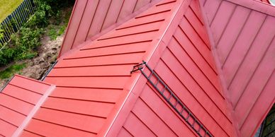 Aerial view of a red metal roof with a chimney and ladder.