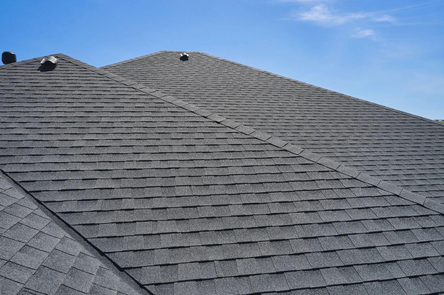 Close-up of a gray shingle roof under a clear blue sky.