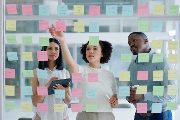Three healthcare professionals  brainstorming using colorful sticky notes on a glass wall.