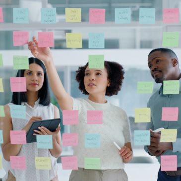 Team brainstorming using sticky notes on glass wall.