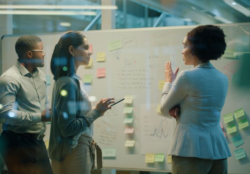 Business people, brainstorming and note on whiteboard for teamwork, planning and invest strategy in office. Data analyst, work and graph for collaboration, meeting and risk management in workplace