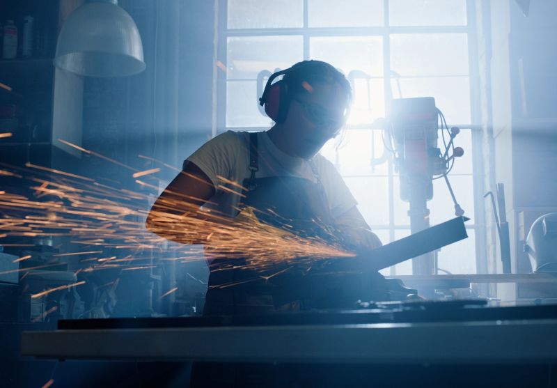 Metal, spark and woman with grinder and iron cutting blade with shadow in a workshop for production. Tools, manufacturing and repair working in an industrial factory with power and electrical machine