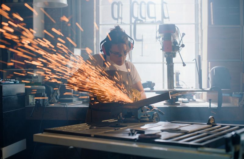 Welding sparks, grinder and woman with metal in workshop for manual labor, material and repair. Factory, steel and person with equipment, tools and machine for manufacturing, maintenance and service