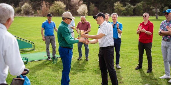 Golf players exchanging trophy on field.