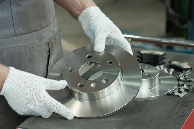 An auto mechanic checks the suspension elements of the car before installation. A new brake disc and a set of brake pads are on the desktop.