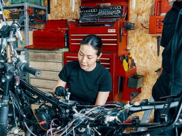 Woman repairing a motorcycle in a workshop filled with tools.