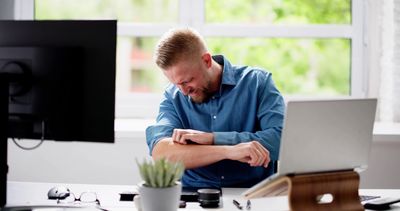A man sitting at a desk scratching his itchy arm.