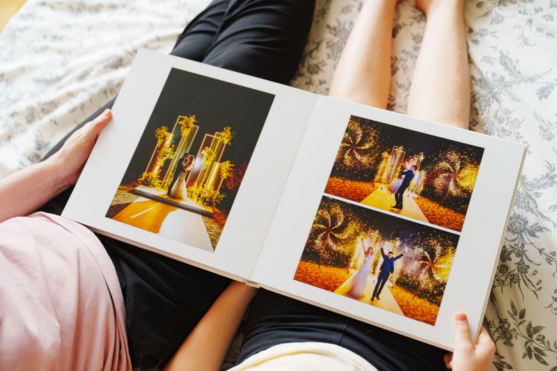 Mom and daughter flipping through a wedding photo book on the bed. Preserving family memories in photos.