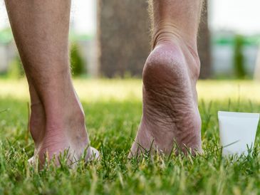 Close-up of feet on grass with a cream tube nearby.
