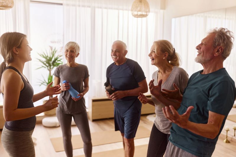 Happy Yoga instructor communicating with group of seniors after having a class in a health club.