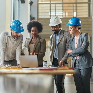 Diverse professionals in hard hats collaborating around a laptop at a construction site.